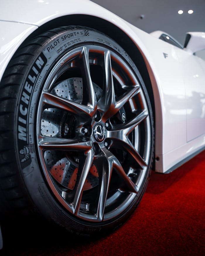 why-choose-us-01 Detailed view of a sports car wheel with reflective chrome rims on a red carpet.