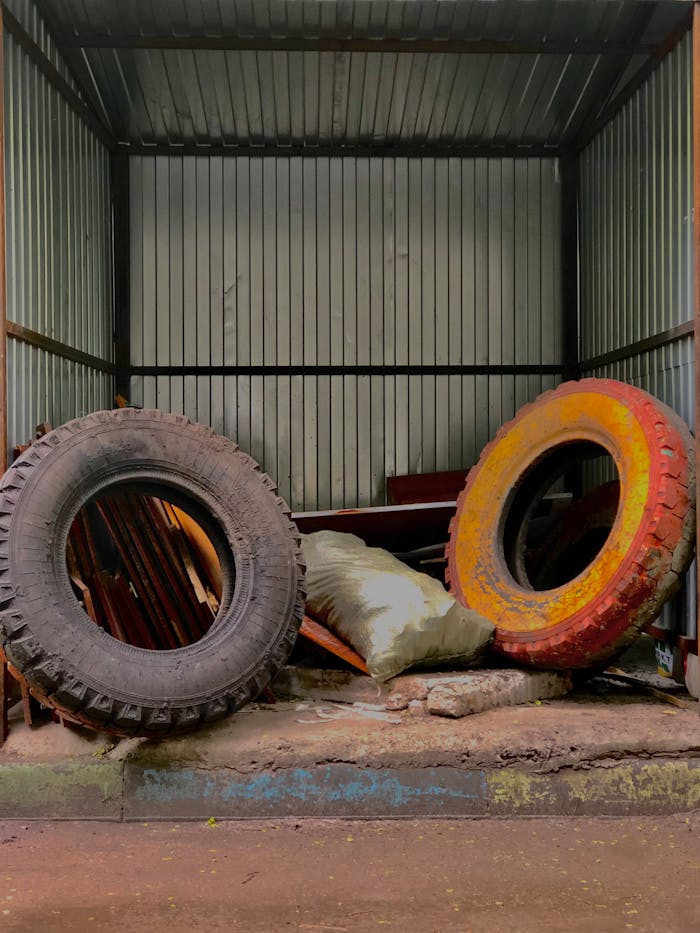 our-story-02 Two large tires in an abandoned garage with metal sheets and old materials.